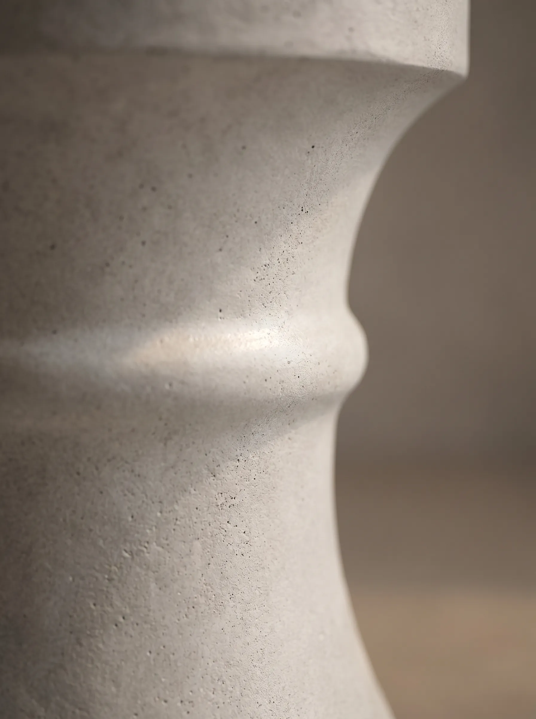 Kum saati sehpa yakın çekim — tornalanmış gövde ve mat beton dokusu
